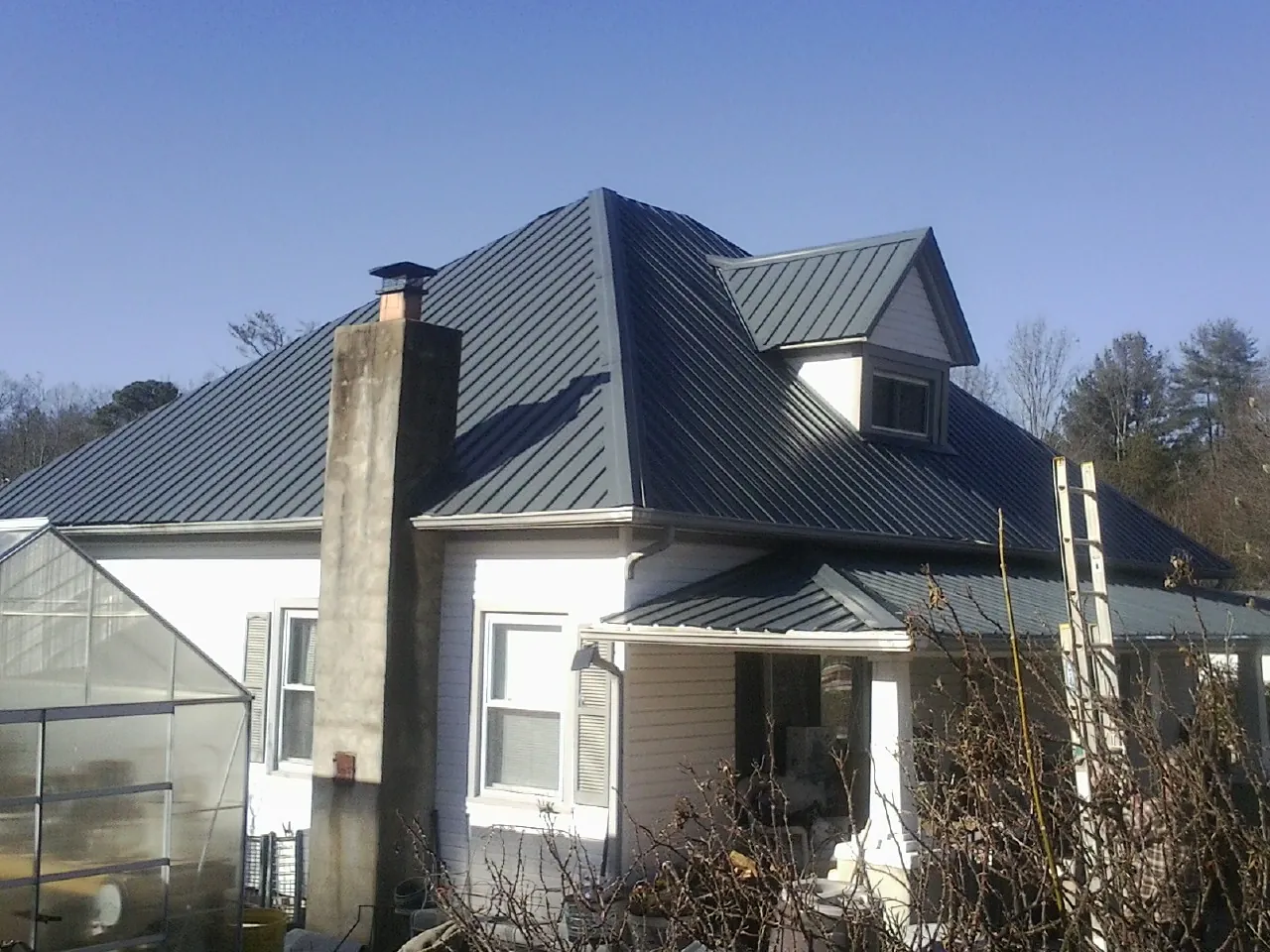 Dark blue standing seam metal roof on a white farmhouse with dormer — Slate & Tile Roof Repair by Roofing Brothers in Burnt Cabins
