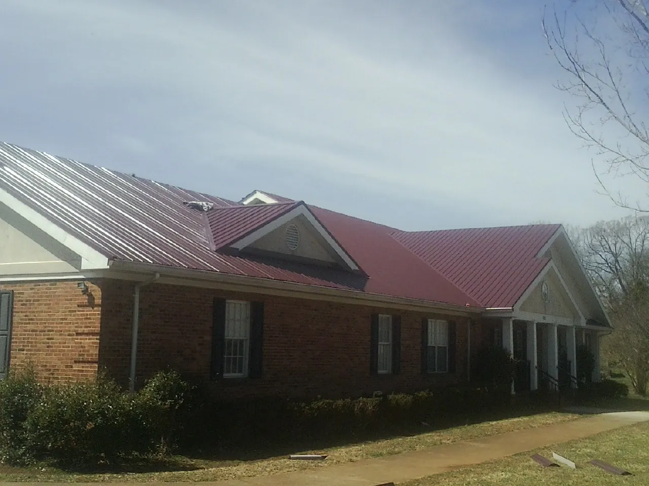 Red metal roof with gabled entries on a long brick building, from a Hail Damage Roof Repair job in Burnt Cabins