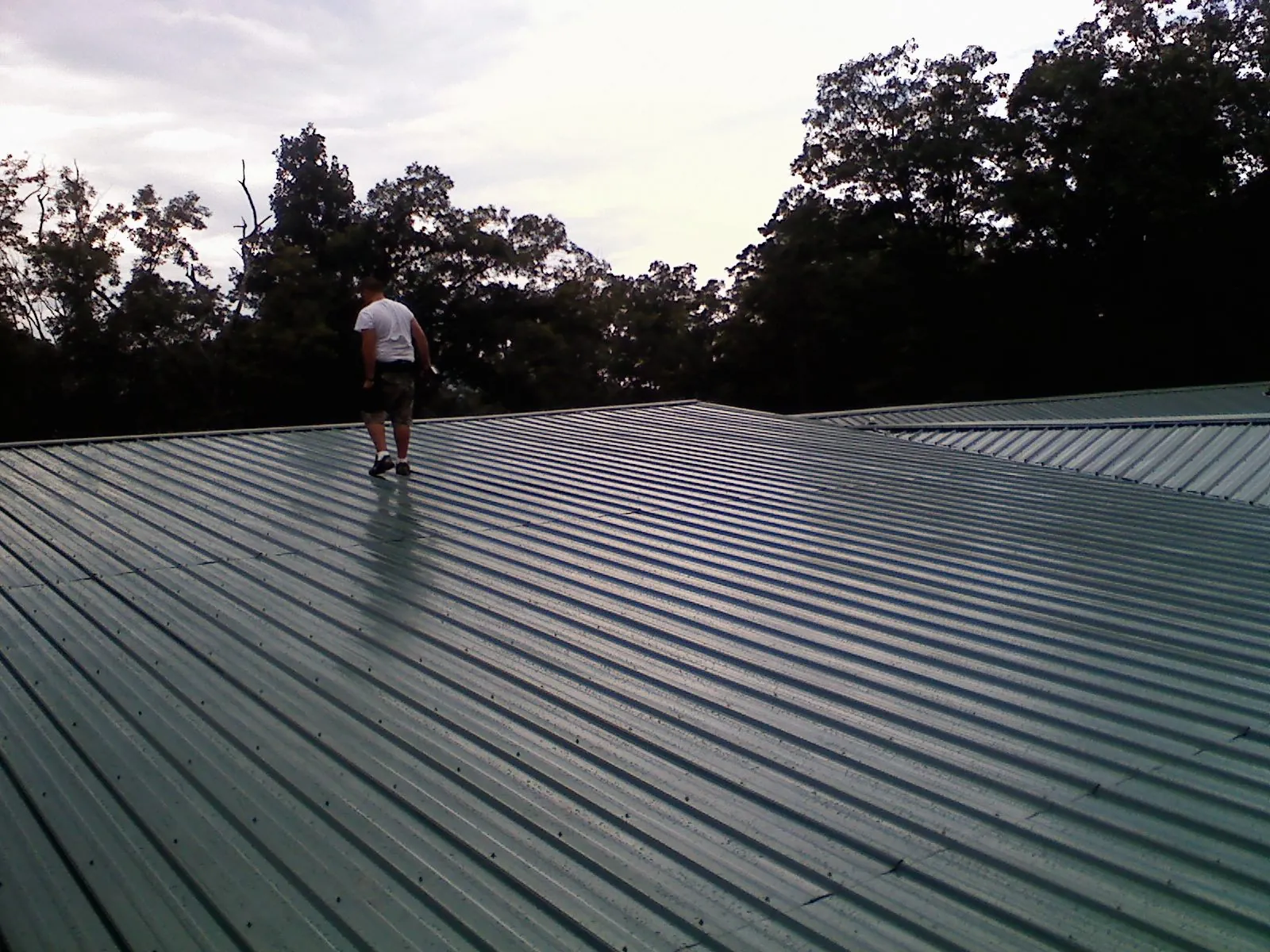 Roofer walking a wide expanse of new green metal roofing in Burnt Cabins