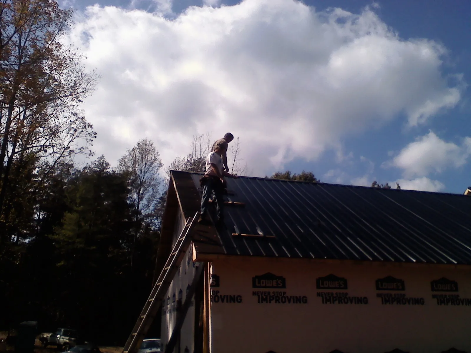 Roofer fastening dark metal panels high against a cloudy sky, from a Roof Inspection job in Burnt Cabins