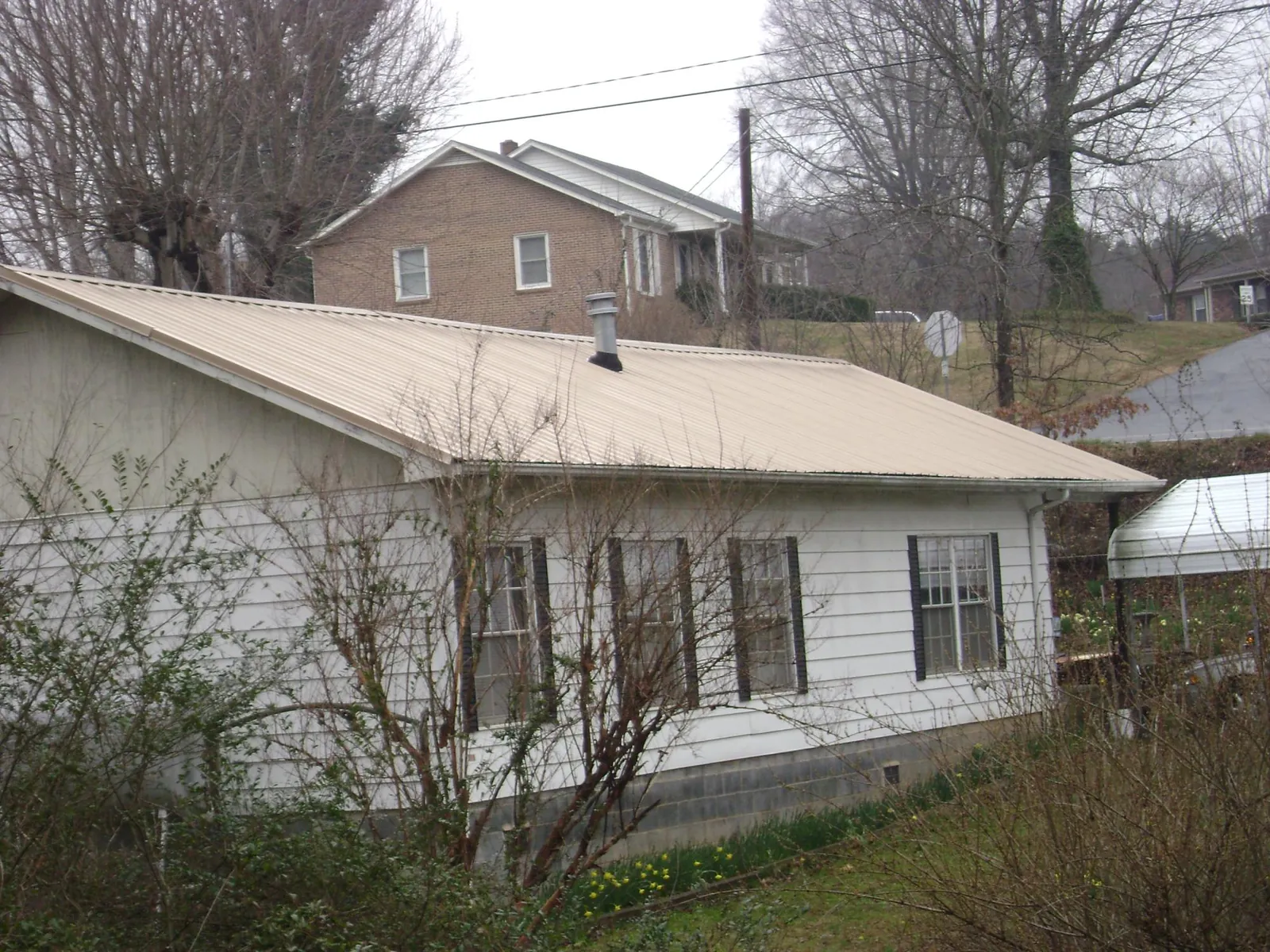Tan metal roof on a white sided house set into a hillside — Commercial Roofing by Roofing Brothers in Burnt Cabins