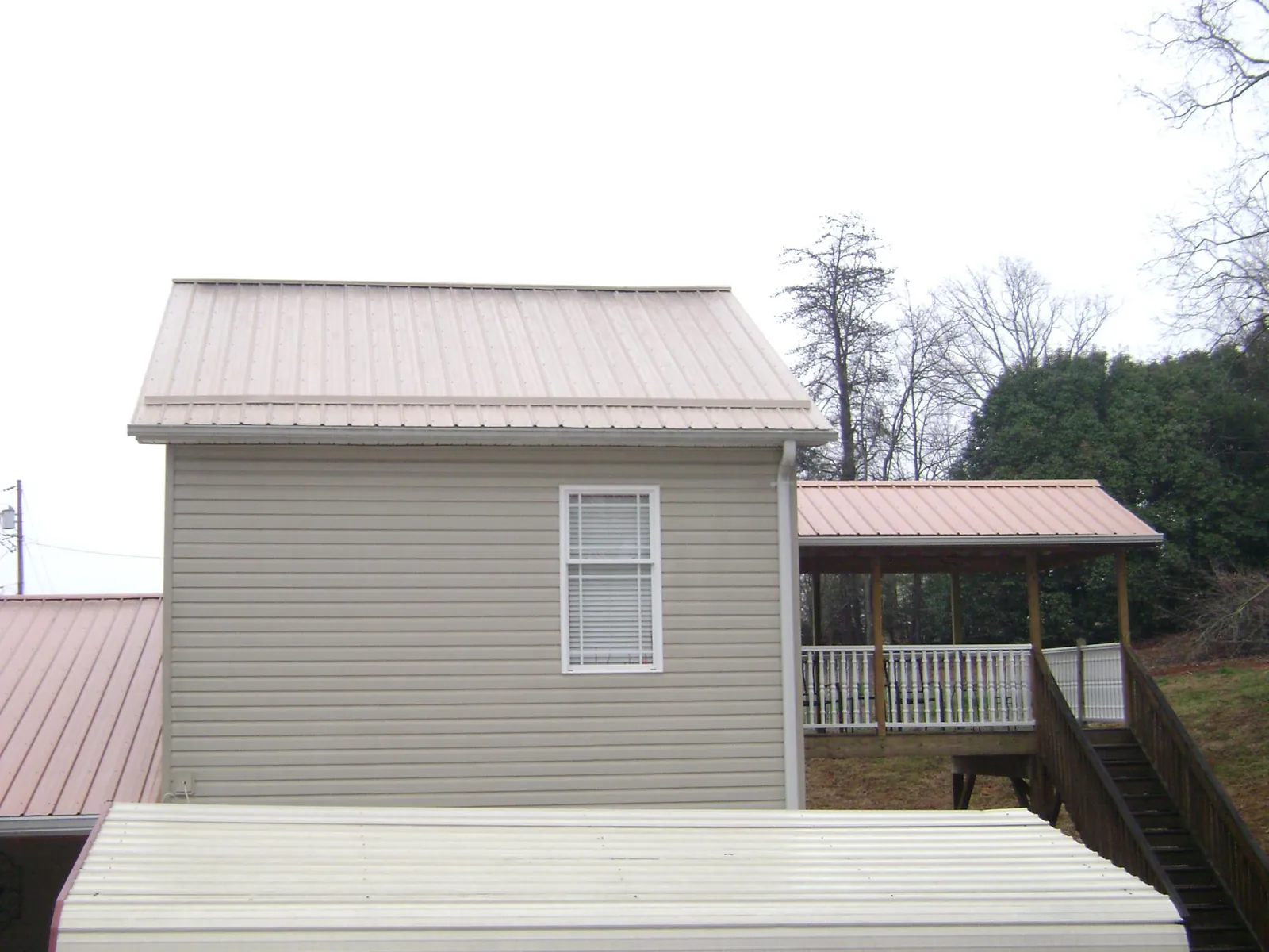 Tan metal roofs on a two story addition and attached porch, from a Roof Replacement job in Burnt Cabins