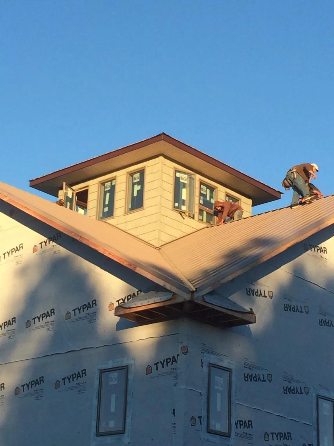 Roofers working around a rooftop cupola on a new metal roof at sunset — Roof Waterproofing in Burnt Cabins by Roofing Brothers